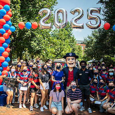 President Gutmann and the Penn Quaker poses with students beneath a 2025 banner